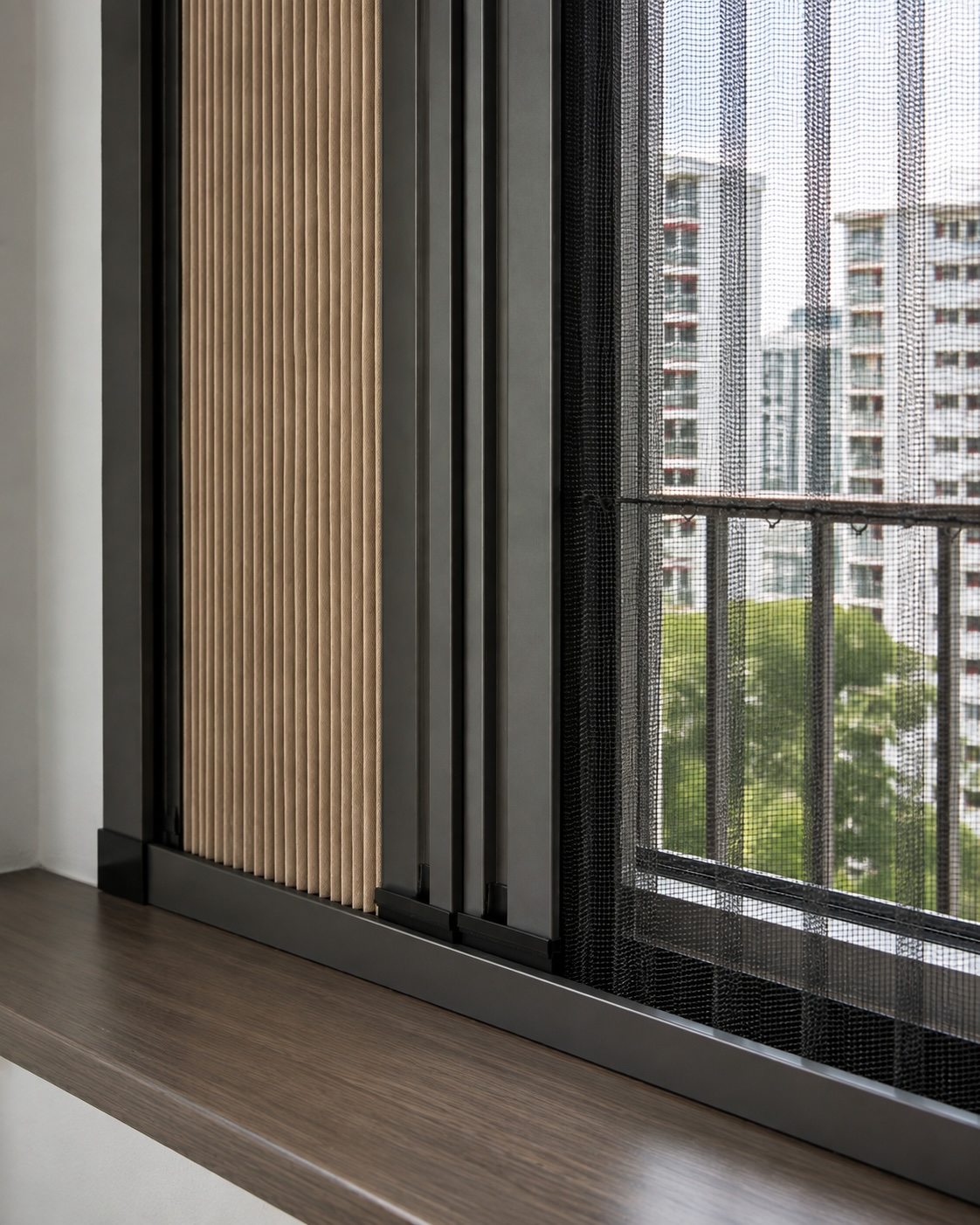 Close-up of the pleated blackout panel, sliding control bars, black insect mesh and slim charcoal frame on a dark wood windowsill, overlooking an HDB estate